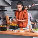 Twee vrouwen in een keuken, met een airfryer mandje vol frietjes op de voorgrond.