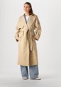 Model draagt een lange beige trenchcoat met ceintuur en blauwe jeans.