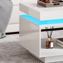 Detail van de witte hoogglans salontafel met blauwe LED-verlichting, een open vak met decoratie en een grijs gestreept tapijt.