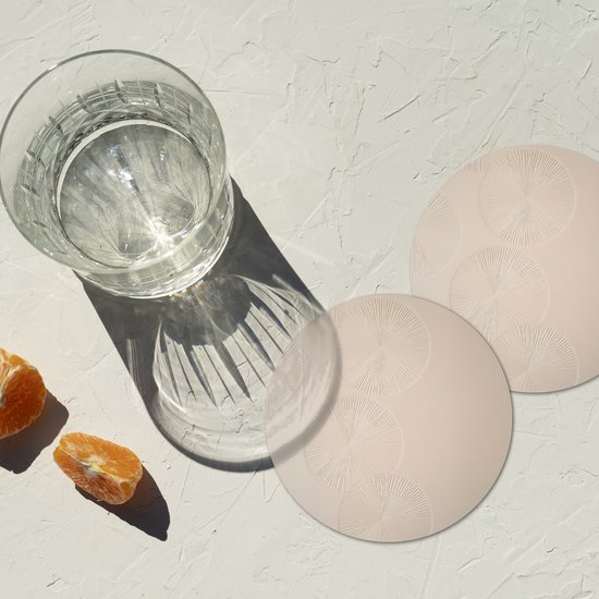 Deux sous-verres ronds beiges à motif de cercles à côté d'un verre d'eau et de quartiers d'orange.