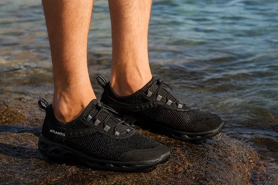 Zwarte Atlantis waterschoenen aan, gedragen door een persoon in het water op rotsen.