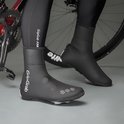 Persoon met zwarte fietsschoenen en "GripGrab" overschoudens, staand naast een racefiets.