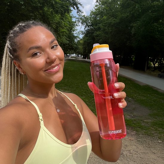 Jeune femme aux tresses blondes tenant une gourde Kambukka rose (1L) avec paille orange.
