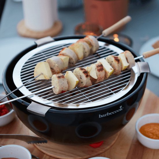 Zwarte tafelgrill met twee spiesjes met worst en stukjes appel, dichtbij.