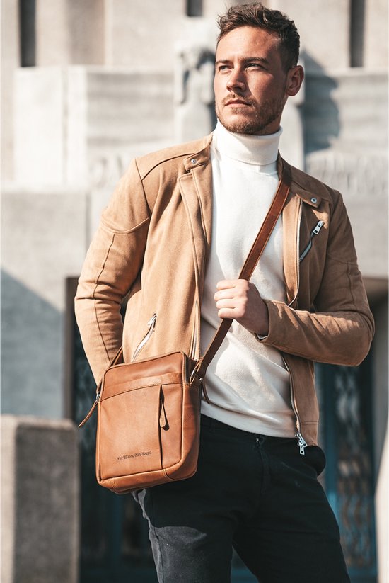 Model met donkerbruine leren schoudertas, gedragen met een bruine jas en witte coltrui.