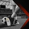 Voeten van een voetballer in witte sportsokken en schoenen op een voetbalveld.