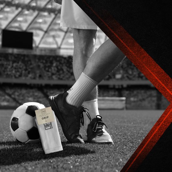 Voeten van een voetballer in witte sportsokken en schoenen op een voetbalveld.