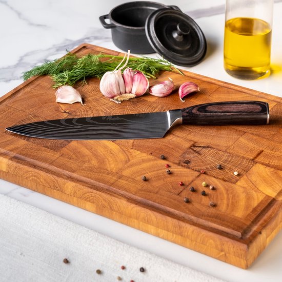 Koksmes met damascus print en donkerhouten handvat op een houten snijplank, met knoflook en dille.
