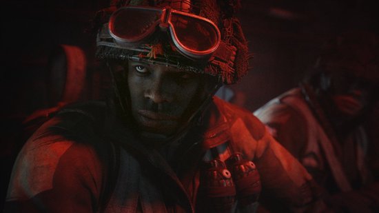 Close-up van een soldaat met een helm en pilotenbril, met rood licht dat op zijn gezicht valt.