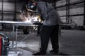 Een lasser in een beschermende outfit last aan een metalen buis in een industriële hal, vonken spatten.