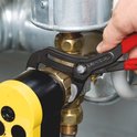 Hand houdt een Knipex Cobra waterpomptang vast, gebruikt op een messing fitting.