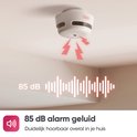 Witte rookmelder aan plafond met rode signaalpijlen. Geluidsgolf met '85 dB alarm geluid'.