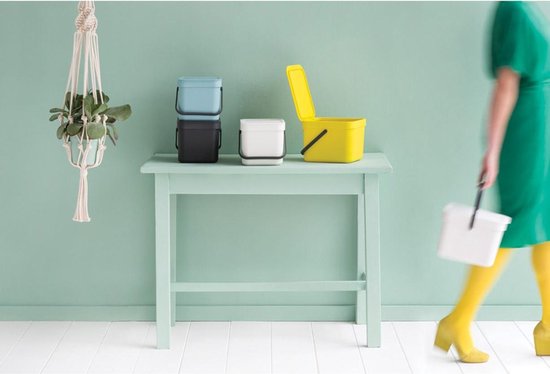 Poubelles bleu clair, noires et blanches sur une table vert menthe. Une poubelle jaune est ouverte.