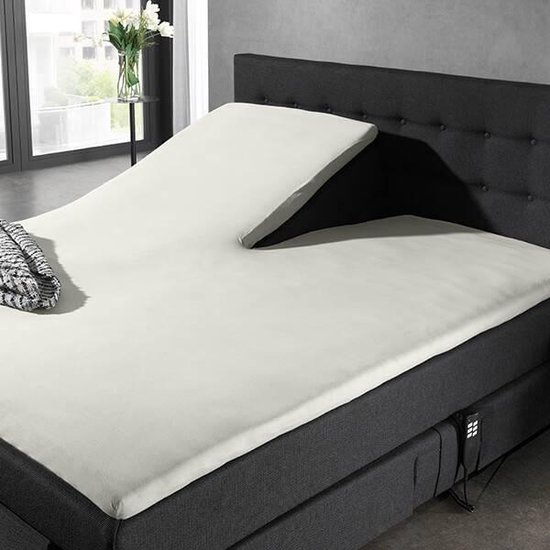 Bed met verstelbaar matras, crème splittopper hoeslaken en donkergrijs hoofdbord, met deken erop.
