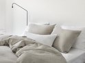 Opgebed en gestyled bed met natuurlijke, beige linnen dekbedden en kussens onder een zwarte lamp.