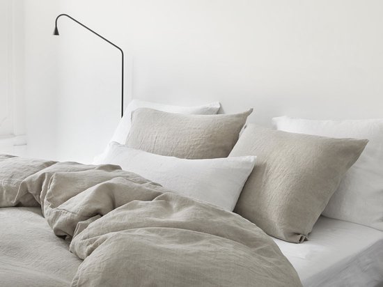 Opgebed en gestyled bed met natuurlijke, beige linnen dekbedden en kussens onder een zwarte lamp.