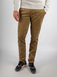Een man met de handen in de zakken van een beige corduroy broek en sneakers.