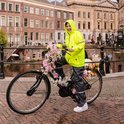 Jong meisje in fluoriserende gele regenjas en grijze regenbroek, staand op een fiets versierd met bloemen.