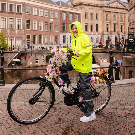 Jong meisje in fluoriserende gele regenjas en grijze regenbroek, staand op een fiets versierd met bloemen.