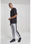 Man in zwart oversized T-shirt en grijze joggingbroek met zwarte streep, poseert met voeten naar voren.