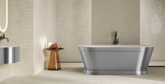 Baignoire ovale autoportante grise avec un bord large et plat. Placee dans une salle de bain aux murs texturés.