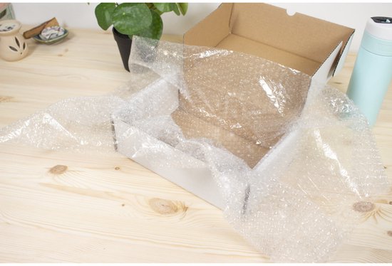 Een witte, geopende kartonnen doos met daarin noppenfolie, op een houten tafel.
