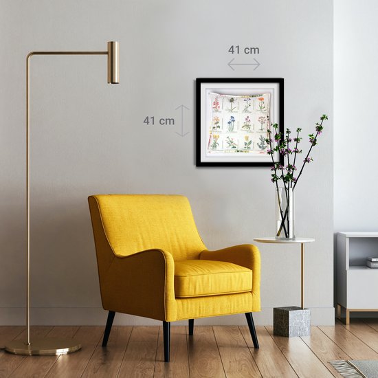 Un fauteuil jaune est placé à côté d'une table d'appoint sur laquelle se trouve un cadre avec des images de fleurs sauvages.