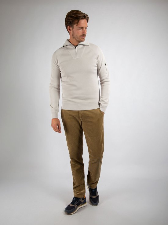 Een man staat met de handen in de zakken van een beige corduroy broek en draagt een gebreide trui.