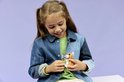 Une fille en veste en jean regarde en souriant un petit hamster LEGO avec une fleur.