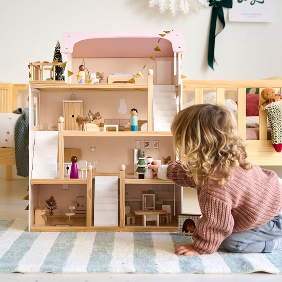 Een klein meisje speelt met een houten poppenhuis met roze dak, aanrecht, tafel en open haard.