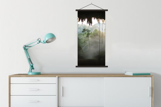 Textielposter met zwarte latten van een grot en regenwoud met mist, boven een kast met lamp.