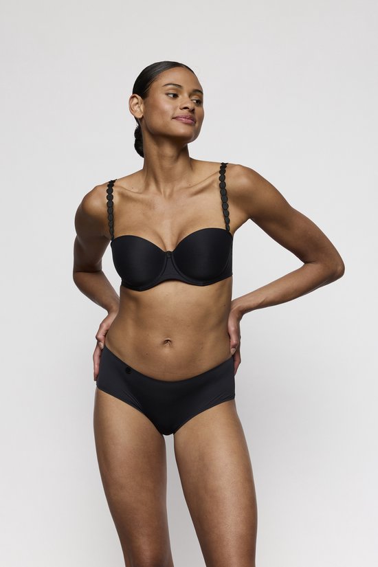 Model met zwarte strapless bh met decoratieve bandjes en bijpassende slip, handen op de heupen.