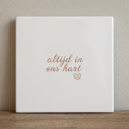Tuile carrée blanche avec le texte 'altijd in ons hart' en lettres fantaisie couleur cuivre, avec un petit cœur en dessous.