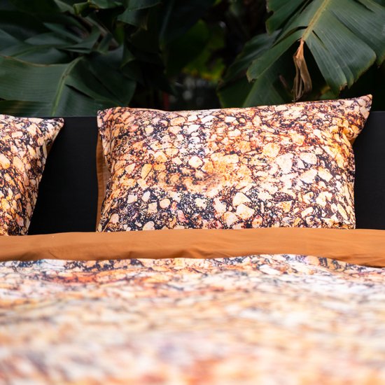 Sluiting op een kussensloop met een gedetailleerde textuurprint in beige, oranje, bruin en zwart.