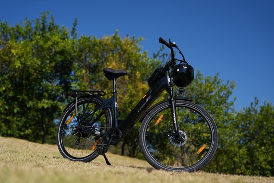 Zwarte elektrische fiets met bagagedrager, staand op een grasheuvel tegen een helderblauwe hemel.
