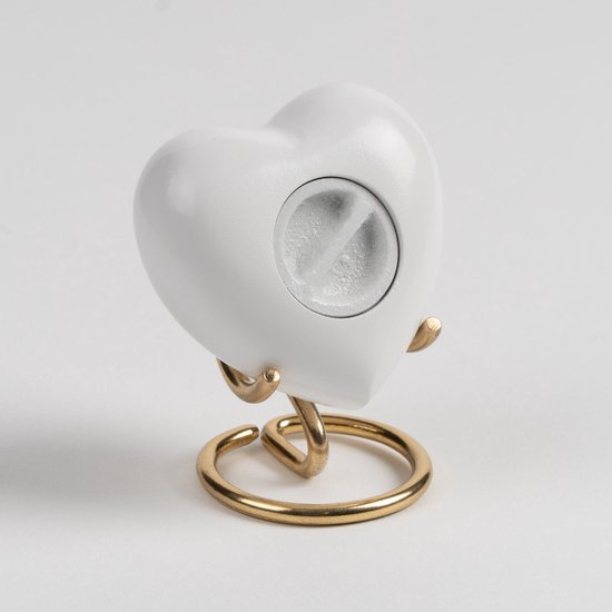 Wit hartvormig urn met gouden standaard en zichtbare opening.