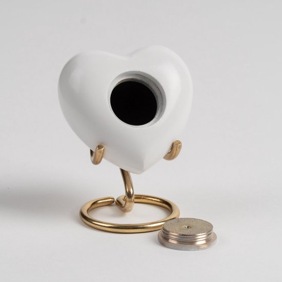 Wit hartvormig urn met gouden standaard en open schroefdop.