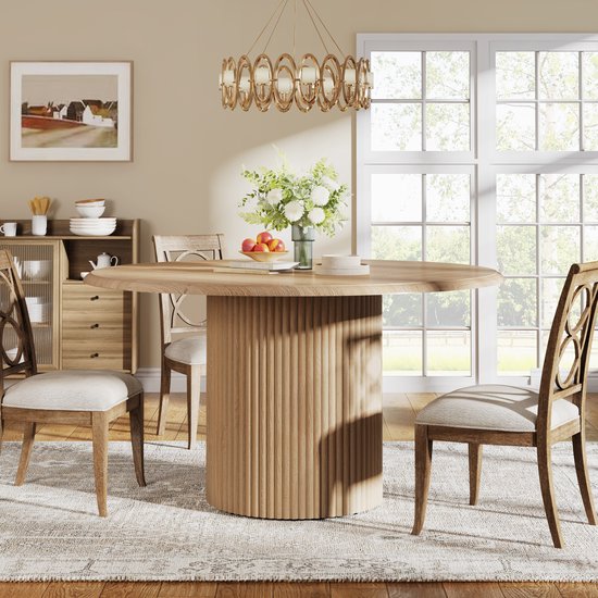 Ronde eettafel met houten visgraatblad en gecanneleerde poot, in een eetkamer met een kast en een kroonluchter.