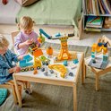 Kinderen spelen met geel bouwspeelgoed met kraan en vrachtwagen.