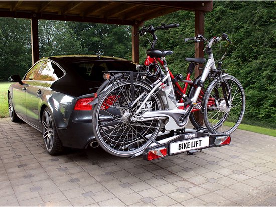 Zwarte auto met een zilverkleurige fietsendrager met twee fietsen erop, onder een afdak.