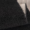 Gros plan d'un tapis noir shaggy, bord replié révélant le dos rayé.