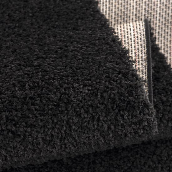 Gros plan d'un tapis noir shaggy, bord replié révélant le dos rayé.