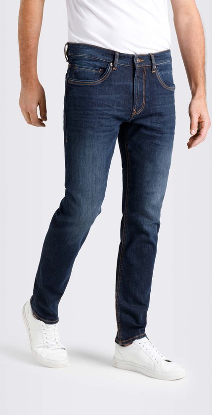 Man in een recht model donkerblauwe jeans. Jeans met oranje stiksels en een lichte wassing op de pijpen, gezien vanaf de zijkant.