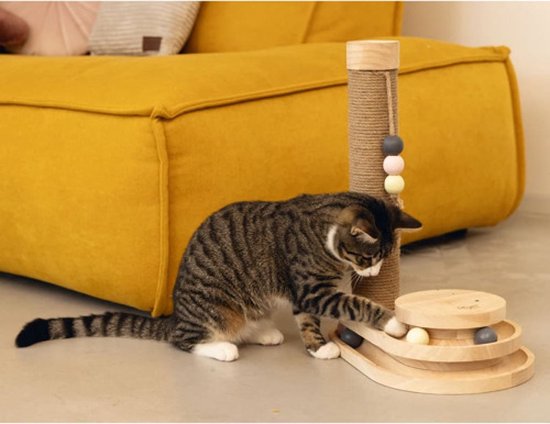 Kattenkrabpaal van hout met jute en speeltoren met balletjes, naast een gele bank. Een gestreepte kat speelt ermee.