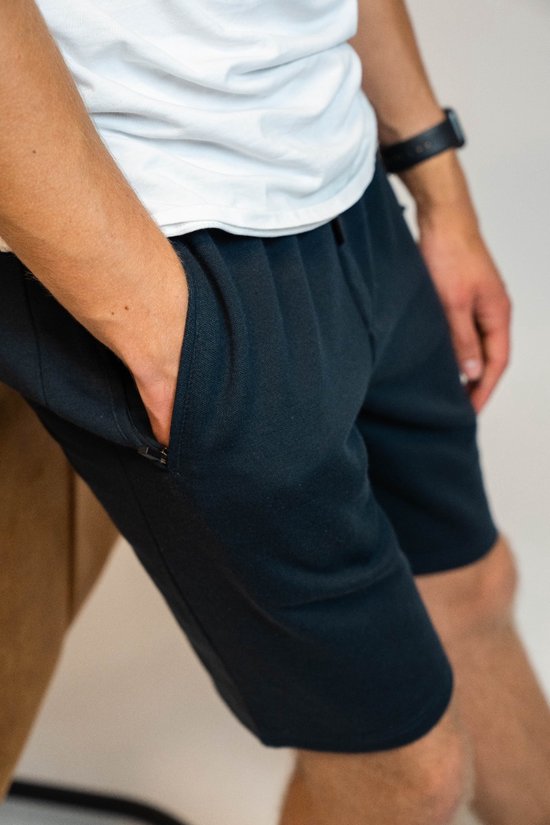 Donkerblauwe korte broek met ritssluiting aan de zijkant, gedragen door een man met zijn hand in de zak.