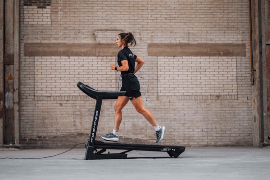 Vrouw rent op zwarte Focus Fitness Jet 4 loopband in industriële setting.