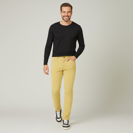 Man met een glimlach draagt een zwarte longsleeve en een gele corduroy broek. Hij draagt zwarte sneakers.