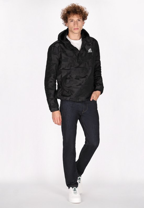 Model draagt een zwarte camouflage jas met capuchon, gecombineerd met een donkere spijkerbroek en witte sneakers.