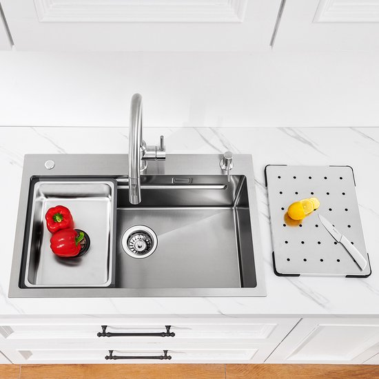 RVS spoelbak met een bakje met rode pepers, kraan, en een snijplank met citroenen en mes.