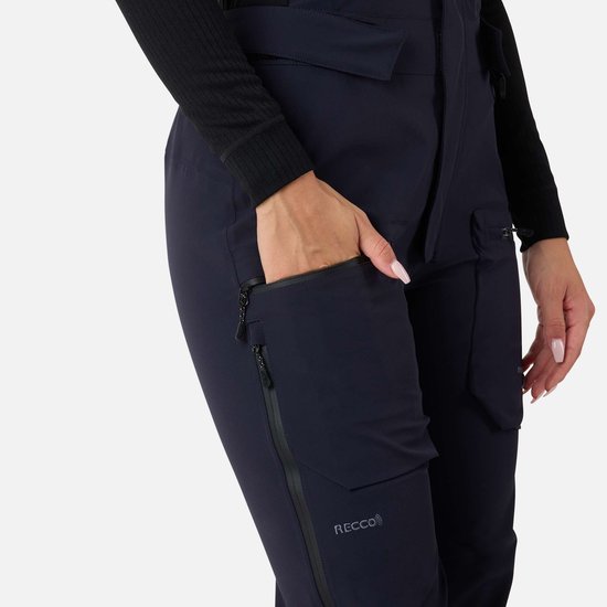 Dichtbij de rechterbroekspijp van een donkerblauwe skibroek, model opent een ritszak.